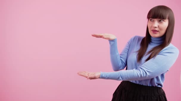 中工作室拍摄的年轻的高加索黑发女人穿着紫色套头毛衣，在粉色背景上显示复制空间. — 图库视频影像