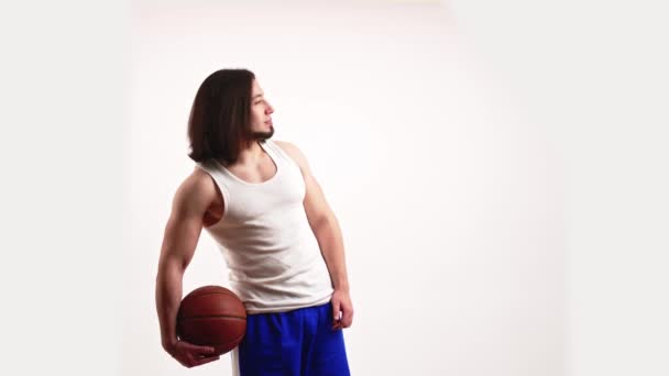 Caucasian bearded muscular man in a sportswear holding basketball ball behind his hip and palm, moving and looking at camera with a smile on his face. Copy space over white background. — ストック動画