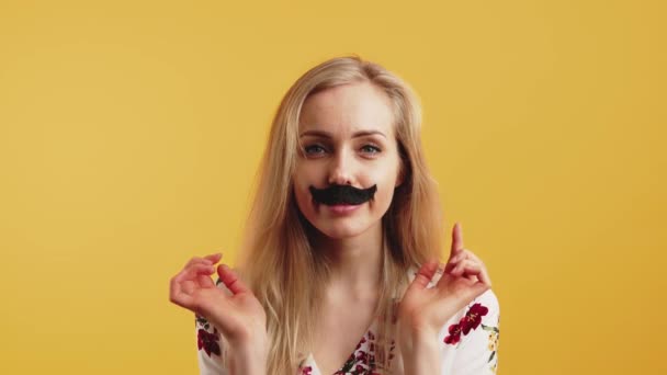 Studio shot of funny humorous blonde caucasian woman with black fake mustache under her nose over yellow background. — Video