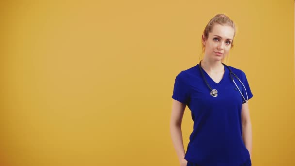 Stolt ung kaukasisk kvinnlig barnläkare läkare bär blå uniform med stetoskop över halsen i studio över orange bakgrund. — Stockvideo