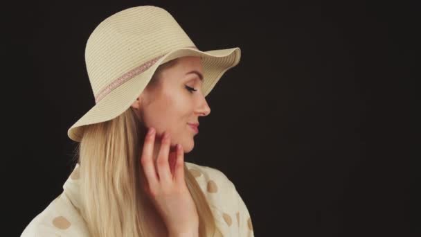 Πλάγια λήψη μιας μυστηριώδους όμορφης καυκάσιας ξανθιάς γυναίκας με καπέλο που αγγίζει το υγιές δέρμα της με το ένα χέρι. Στιγμιότυπο στούντιο σε μαύρο φόντο. — Αρχείο Βίντεο