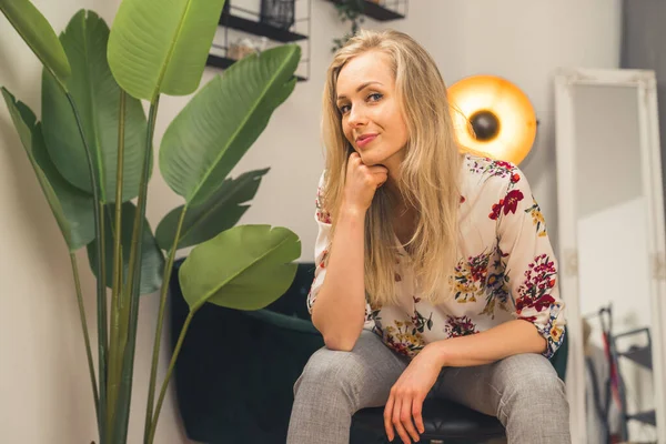 Relaxed confident beautiful blonde woman in her 20s or 30s sitting casually and looking at camera in her modern apartment. — 스톡 사진