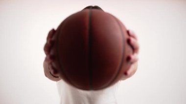 Basketbol topunun arkasına saklanan uzun saçlı Avrupalı sakallı adam ara sıra kameraya bakıyor. Portre stüdyosu beyaz arka planda çekildi.