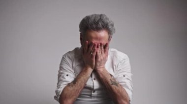 Yorgun yaşlı adam yüzünü ovuyor ve kameraya bakıyor.