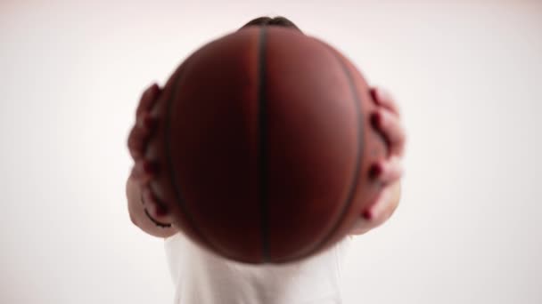 European bearded man with long hair hiding behind basketball ball and looking at camera from time to time. Portrait studio shot over white background. — Stock Video