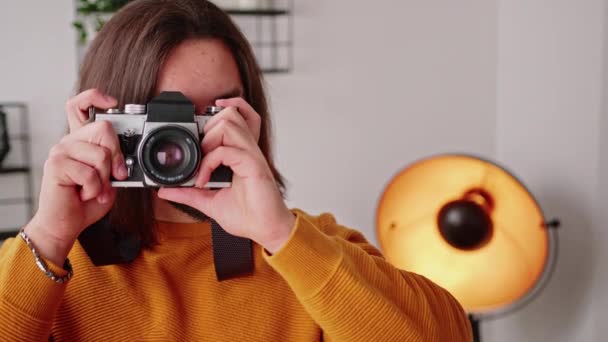 Barbudo caucásico de pelo largo freelancer chico tomando fotos con su cámara y mirando a la cámara con una sonrisa en la cara. — Vídeo de stock