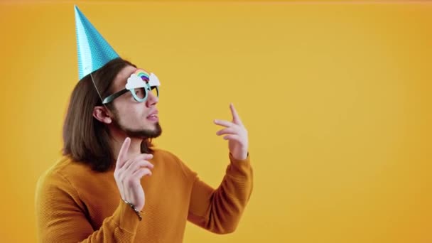 재미있는 코카서스 중년의 수염 남자가 거대 한 생일 컵 과 무지개가 달린 특이 한 안경을 쓰고 춤을 추고 있다. 스튜디오 촬영. 생일 파티 개념. — 비디오