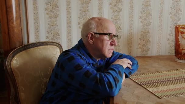 Starší muž se dívá z okna, opíraje se o stůl — Stock video