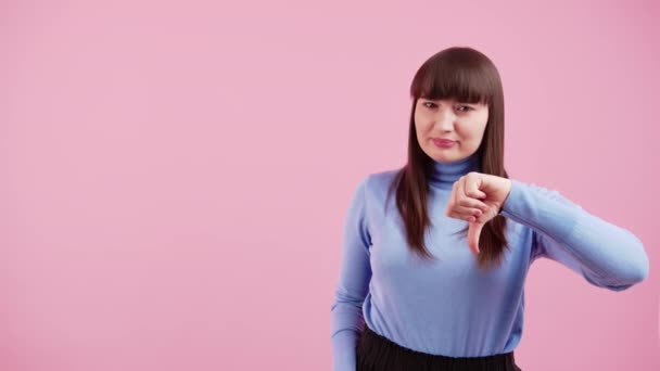 Krásná atraktivní brunetka žena 20s v modrém rolnech svetr stojící pózuje ukazující palec dolů izolované na růžové barevné pozadí stěny, studiový portrét, copyspace — Stock video