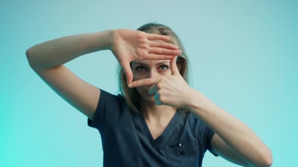 Blonde jeune femme caucasienne faisant cadre avec les mains et les doigts sur fond bleu turquoise. Plan studio moyen. — Video