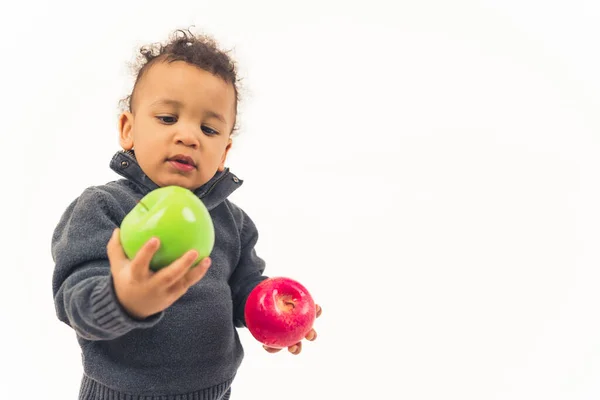 Bébé garçon avec les cheveux bouclés regardant la pomme verte juteuse dans une main et tenant la pomme rouge dans l'autre. Concept d'alimentation saine. — Photo