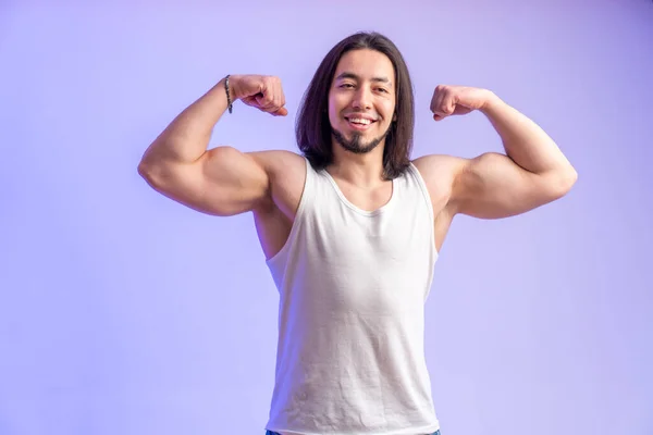 Young athletic man showing biceps and smiling and looking away studio shot medium shot isolated purple background indoors copy space — Stockfoto