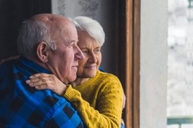 satisfied senior couple embracing and looking children in the garden from the window senior people support concept medium closeup indoors