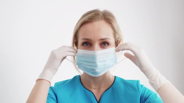 Відповідальна біла жінка-лікар одягає її захисну маску перед операцією. Портрет крупним планом на білому тлі . — стокове відео