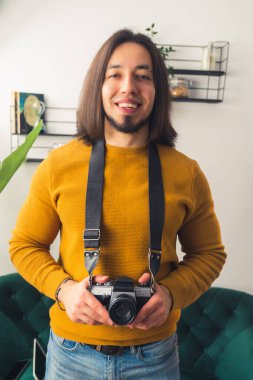 Çekici genç fotoğrafçı bir kamera tutuyor ve gülümsüyor, gündelik kıyafetler orta boy. 