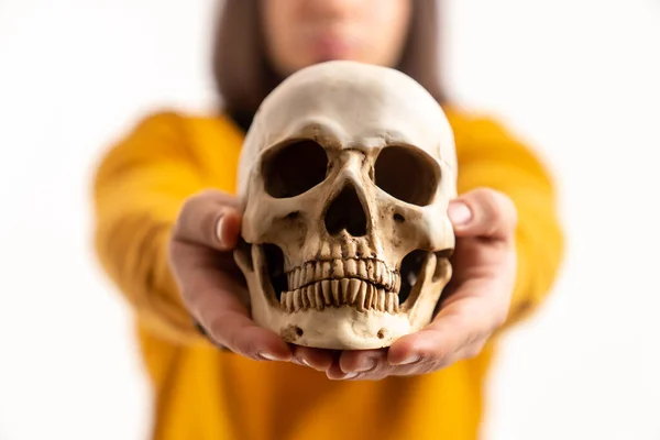Young dark-haired man showing fake skull to the camera white background studio shot — Stockfoto