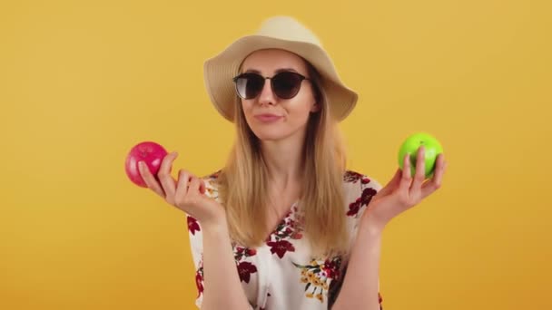 백인젊고 아름다운 아가씨가 선글라스를 쓰고 두 개의 사과중 선택하는 모자를 쓰고 있다 — 비디오