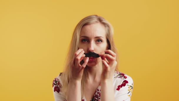 Happy young woman putting on fake mustache, isolated orange background — стоковое видео