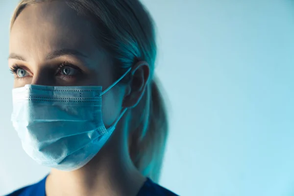 Retrato de uma bela loira jovem enfermeira caucasiana com uma máscara cirúrgica closeup fundo azul estúdio tiro conceito médico — Fotografia de Stock