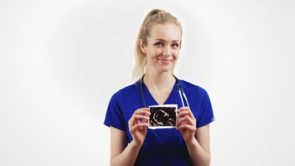 Yakında anne olacaksın. Elinde orta boy bebek ultrasonu olan beyaz arka plan stüdyosu fotokopisi çeken genç bir hemşire. — Stok video