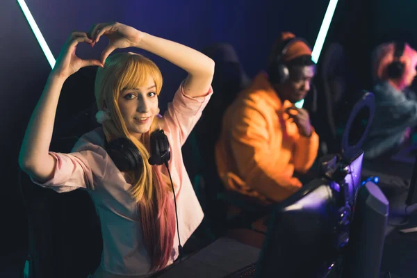 Young caucasian adorable female gamer influencer showing heart gesture with two hands and looking at camera. Internet cafe concept. —  Fotos de Stock