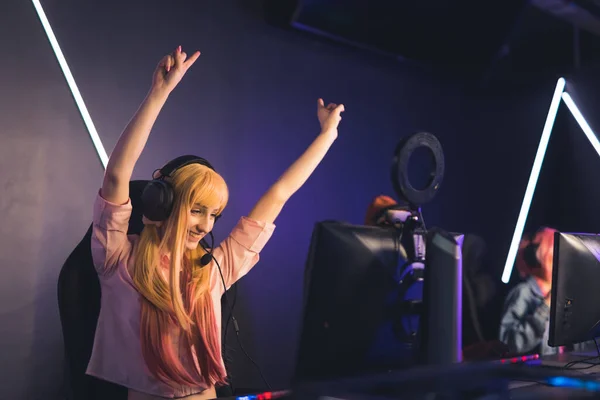 Victory. Excited satisfied long-haired female gamer influencer wins her next online match in a tournament. Happiness shown by throwing hands in the air. Internet cafe. —  Fotos de Stock