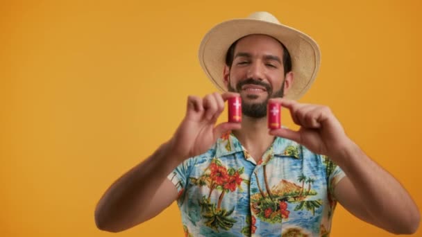 Sexy séduisant homme barbu confiant en tenue de vacances tenant deux piles rouges et les montrant à l'appareil photo sur fond orange. Concept d'écologie. — Video