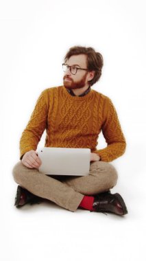 Genç adam yerde oturuyor ve dizüstü bilgisayarında çalışıyor. Tam çekim stüdyosu dikey video beyaz arka plan. 