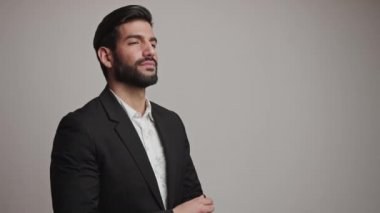 Koyu saçlı yakışıklı sakallı Kübalı adam gri arka planda smokin bilekliğini düzeltiyor. Orta stüdyo çekimi..