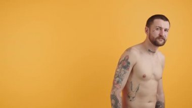 Turuncu arka planda duran yakışıklı, sakallı, beyaz bir gencin portresi.