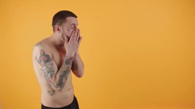 Beyaz bir adam kameranın önünde yüzünü siliyor.