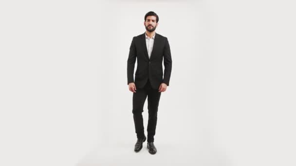 Handsome fit confident bearded Cuban man in a black suit posing in a studio over white background, shushing the camera with his finger in seductive way. — Vídeos de Stock