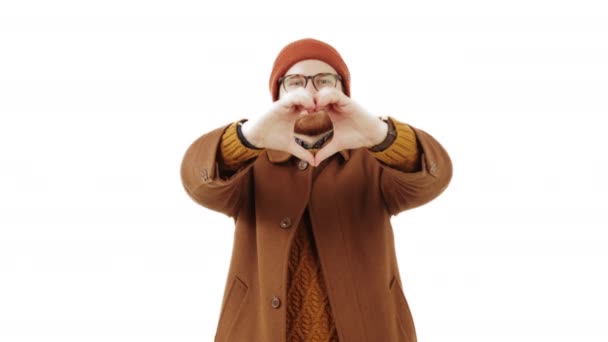 Young Caucasian man making a heart shape with fingers expressing love and positive feeling medium shot isolated studio shot love concept — Stock Video