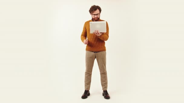 Full shot of a young bearded man standing and working in laptop studio shot isolated copy space job concept — стоковое видео