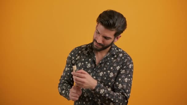 Handsome sexy Latin American bearded man with beautiful white teeth holding a bamboo toothbrush studio shot orange background. Ecological hygiene concept. — Stock Video