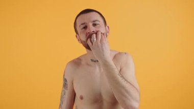 Genç ve çekici sakallı adam bıyığını turuncu arka planda büküyor.