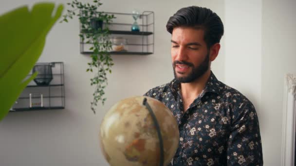 Bonito homem cubano barbudo intrigante com cabelo preto brilhante girando globo de plástico ao redor, planejando suas viagens futuras, e sorrindo. Conceito de viagem. — Vídeo de Stock
