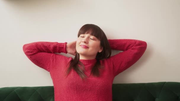 Mujer caucásica relajándose y estirándose en el sofá mientras toma un descanso — Vídeos de Stock