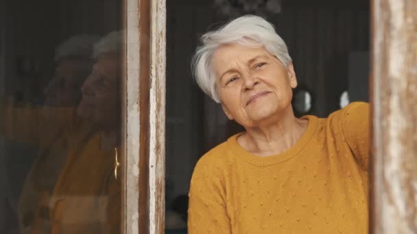 Зрелая белая женщина с седыми волосами, смотрящая через окно, копирует космическую среду крупным планом — стоковое видео