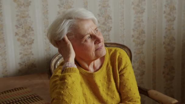 Senior woman sitting on the chair and looking out of the window while leaning her head on hand and straightening her hair — ストック動画