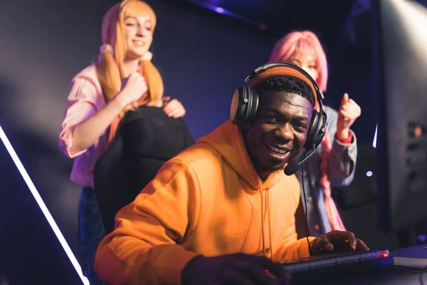 Afro-American young man looks at the camera wearing headphones, two girls standing behind copy space —  Fotos de Stock