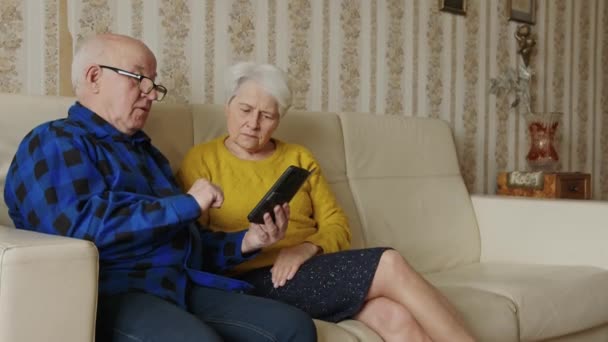 Senior cheerful couple using smart phone in the living room, slowmotion horizontal — Stock video