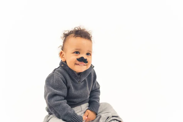 Mignon petit enfant heureux portant une fausse moustache et assis sur le sol, fond blanc isolé — Photo