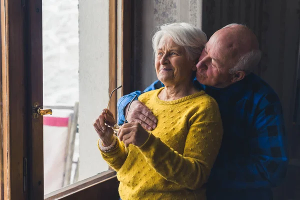 Senior man embracing senior woman near window senior people support concept room indoors medium shot — ストック写真