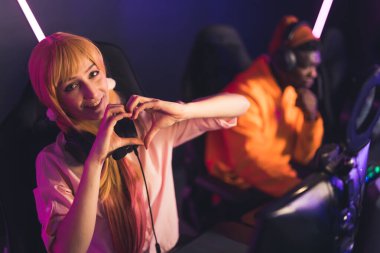 Modern teknoloji ve eğlence aktivitesi. Sevimli genç Avrupalı oyuncu kız kameraya kalp hareketi yapıyor ve gülümsüyor, bir internet kafede iken..