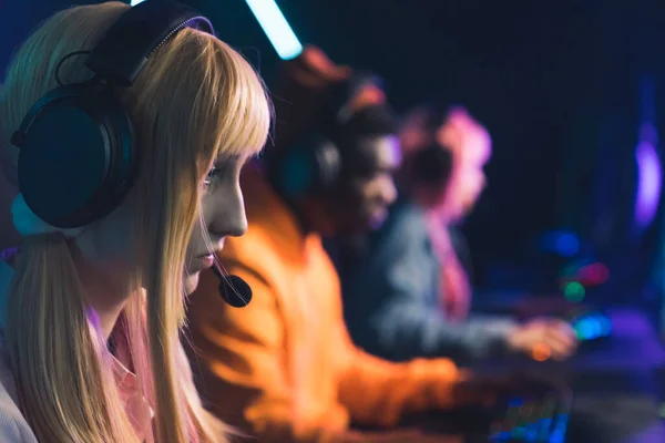 Group of online gamers, focus on the foreground. Beautiful blonde twenty-year-old gamer girl fighting in a tournament. — стоковое фото