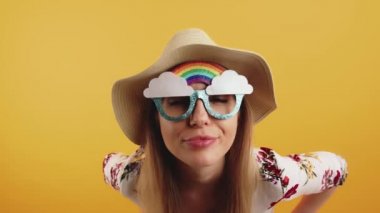 Gökkuşağı güneş gözlüklü genç sarışın kadın kameraya bakıyor.