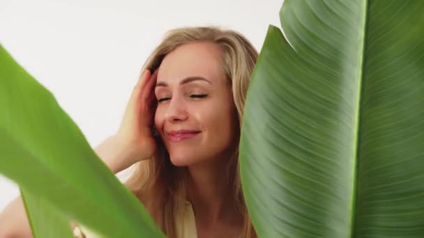 Młody jouful blondynka kobieta pozowanie behing w zielony roślin zbliżenie studio strzał biały tło piękno koncepcja — Wideo stockowe
