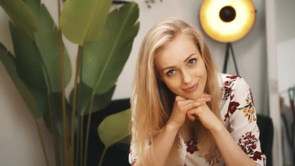 Γοητευτική ξανθιά νεαρή γυναίκα κοιτάζοντας την κάμερα και χαμογελαστό σαλόνι μεσαίου closeup έννοια του τρόπου ζωής σε εσωτερικούς χώρους — Αρχείο Βίντεο