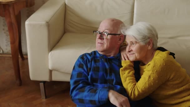 Starší manželé pár sedí na podlaze, dívá se jinam a objímání kopírování tempo obývací pokoj pozadí — Stock video